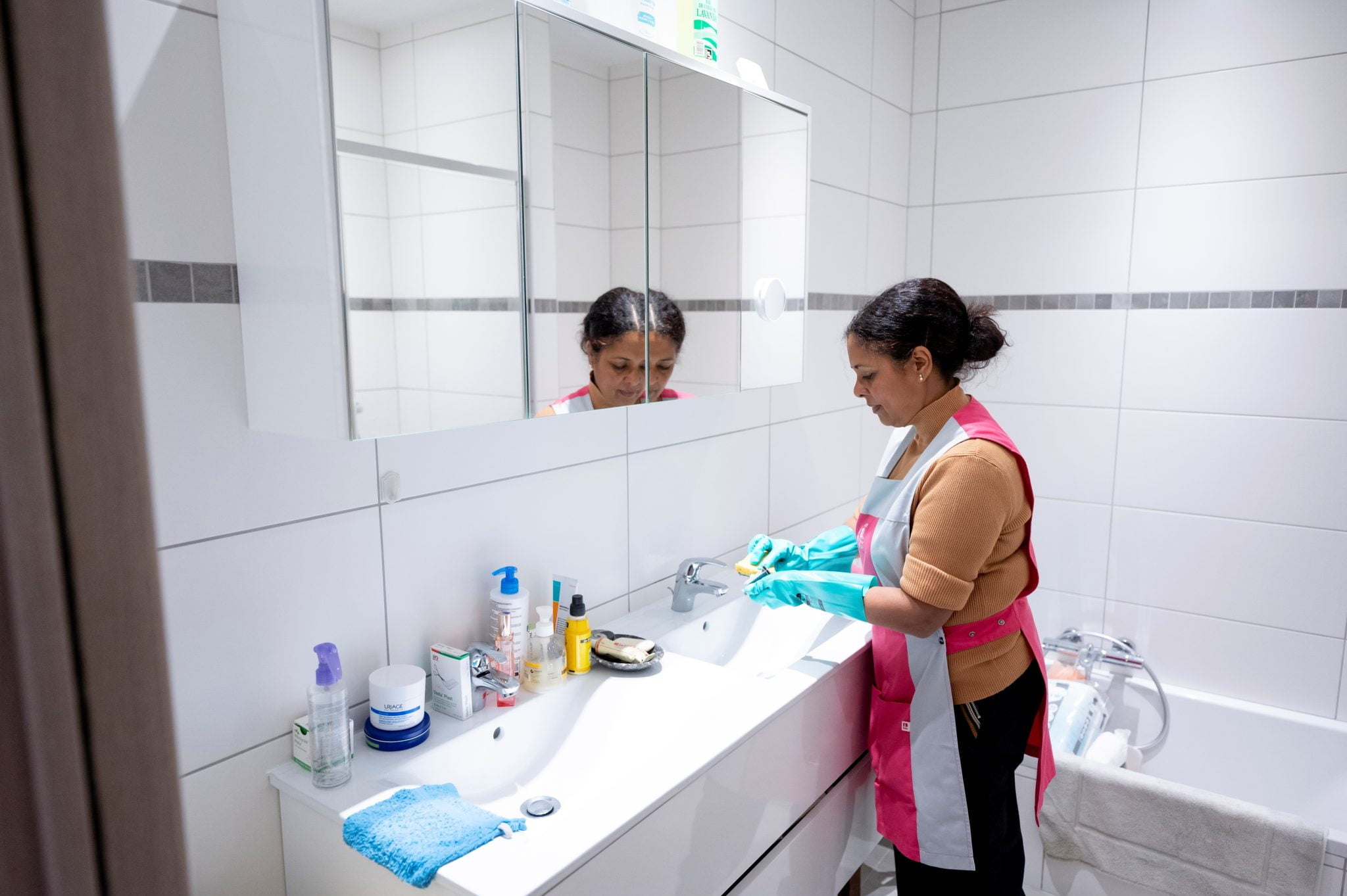 L'Aide Ménagère Sociale, à l'aide d'une éponge, nettoie les éviers de la salle de bain.